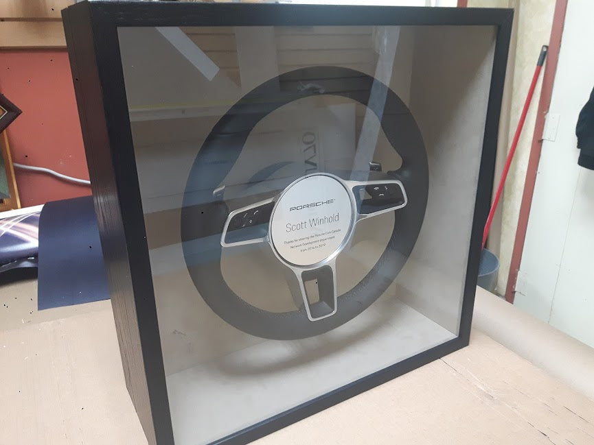 Porsche steering wheel displayed in a custom shadowbox frame with black suede matting by Framing & Display.